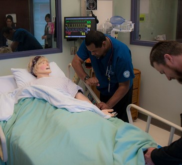 Nursing students checking vitals on practice dummy.