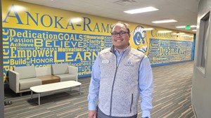 Person standing in front of a colorful mural at Anoka-Ramsey Community College, smiling.