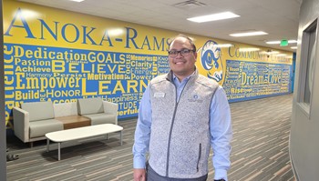 Person standing in front of a colorful mural at Anoka-Ramsey Community College, smiling.