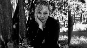 Person with short hair, leaning on their hand, smiling gently while sitting in a park.