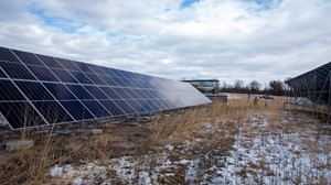 Rows of solar panels in a field with light snow cover under a cloudy sky.