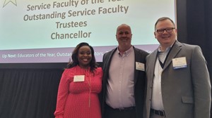 Three individuals smiling and standing in front of a presentation screen at an academic event.