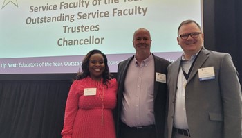 Three individuals smiling and standing in front of a presentation screen at an academic event.