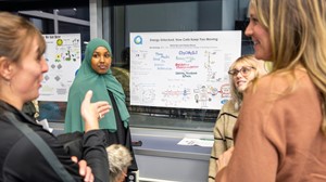 Four individuals are engaged in a discussion in front of a whiteboard covered with scientific diagrams 