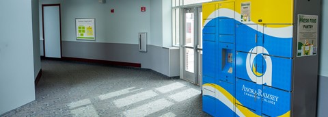 Interior of a corridor at Anoka-Ramsey Community College with bright sunlight shining through windows and a blue and yellow fresh food pantry.